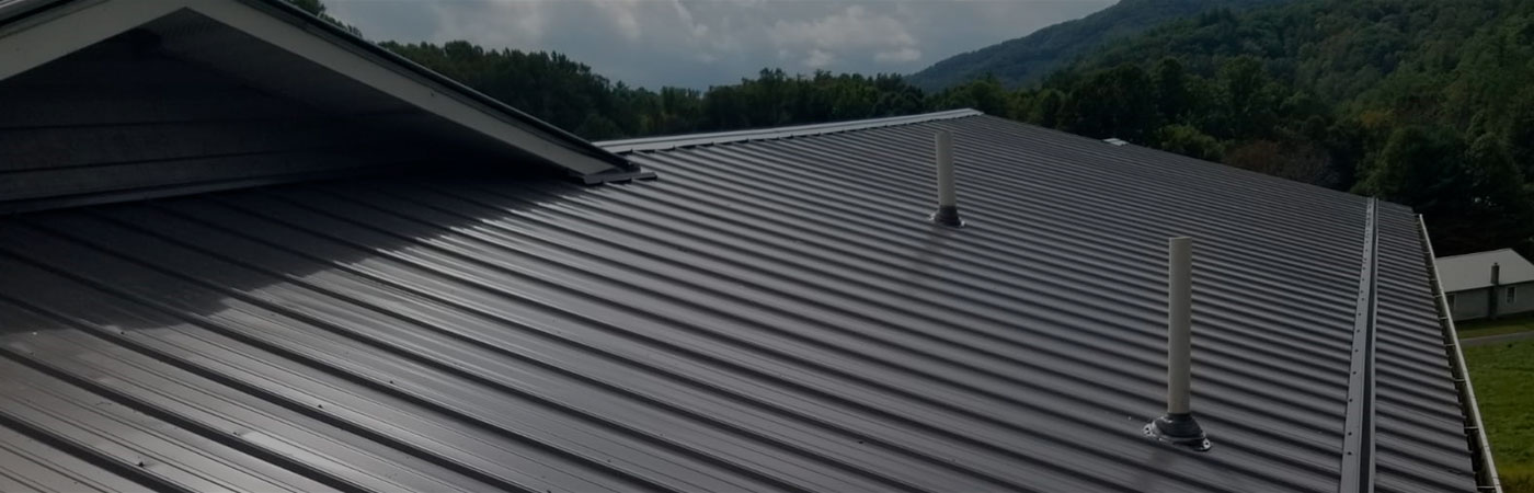 A sleek metal roof with pipes against a cloudy sky and forested hills.